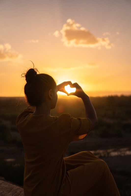 An image of a girl with her hands making a heart shape against the night sky to talk about how to start loving yourself.