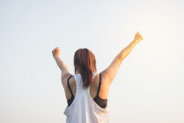An image of a girl with her hands in the air because she feels empowered from working with a health and wellness coach.