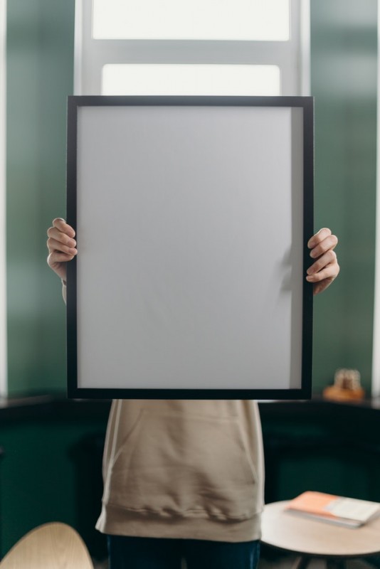 An image of a girl holding a frame in front of her face as a symbol to discuss making yourself into the person you want to be.