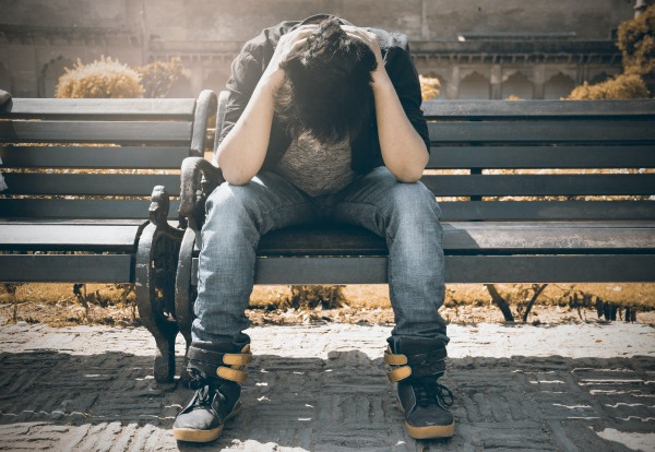 An image of a stressed man with his hands on his head sitting on a bench to talk about how diet and mental health are connected. who is