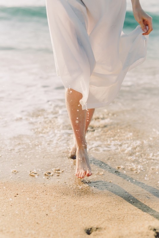 An image of a person walking through the sand barefoot to talk about the benefits of grounding.