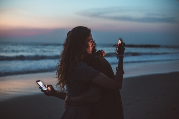 An image of a couple hugging while looking at their phones to talk about the health issues associated with social media and how it distracts people.