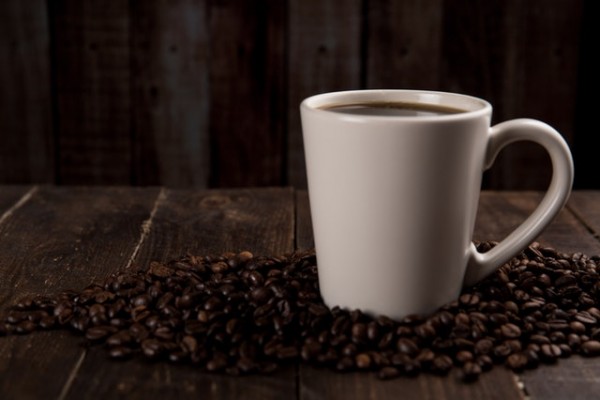 An image of a coffee cup with coffee beans around it to discuss the benefits of coffee for managing pain.