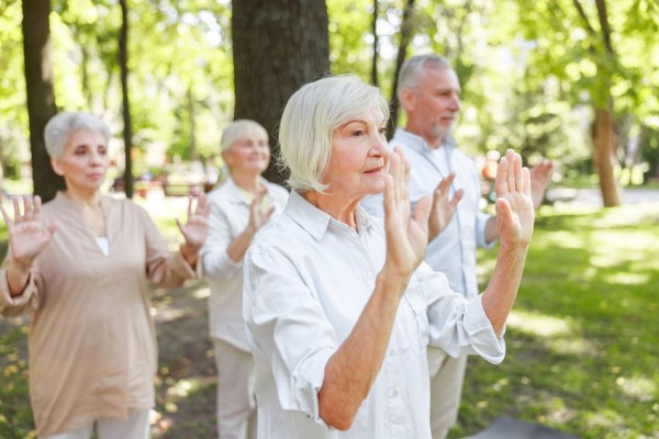 An image of a few senior citizens practicing Qigong exercises in a forest area.
