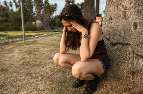 Image of a girl stressed holding her head while leaning against a tree.