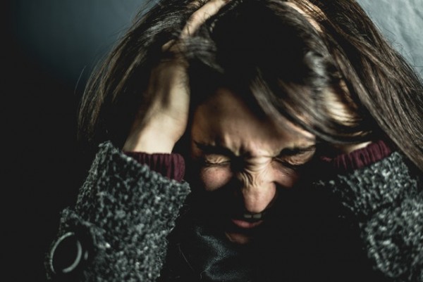 A person overwhelmed with a scrunched face and hands in her hair.